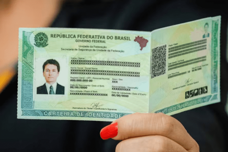 Mão feminina com unhas vermelhas segurando a nova Carteira de Identidade Nacional aberta, exibindo foto, dados e QR Code.