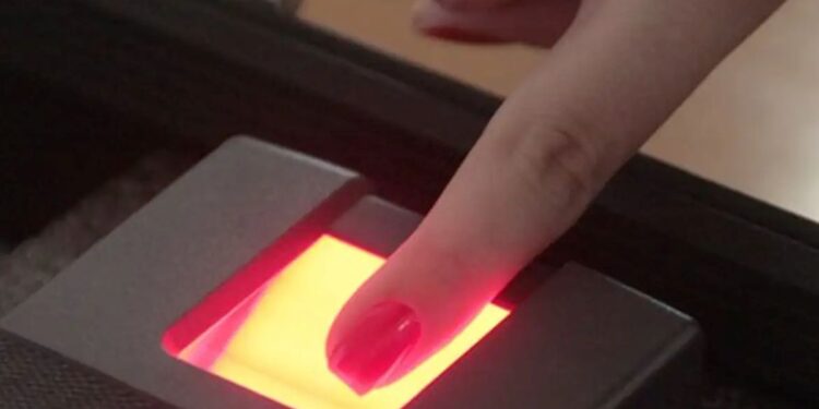 Mão posicionando dedo em leitor biométrico com luz verde