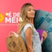 Uma jovem estudante sorridente com mochila bege nas costas e segurando livros roxos. Ao lado, o logotipo colorido do programa Pé-de-Meia com o slogan "A poupança do ensino médio" sobre um fundo rosa. No fundo, notas de 100 reais dispostas em leque.