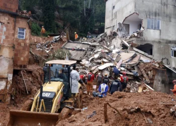 Equipe de bombeiros e retroescavadeira CAT trabalham nos escombros de casas destruídas por deslizamento de terra.