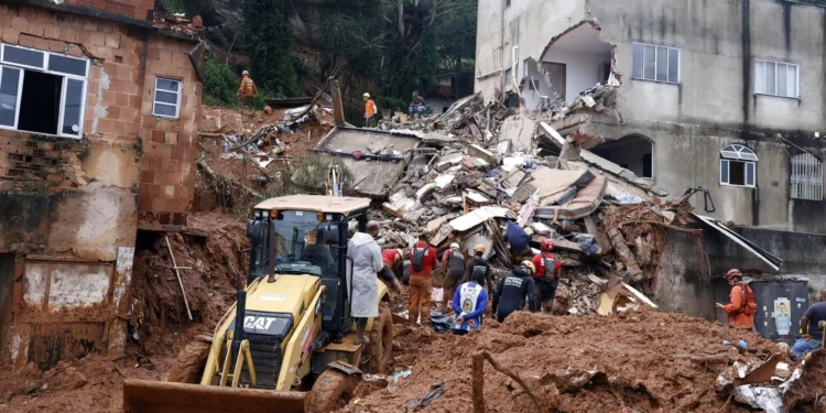 Equipe de bombeiros e retroescavadeira CAT trabalham nos escombros de casas destruídas por deslizamento de terra.