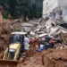 Equipe de bombeiros e retroescavadeira CAT trabalham nos escombros de casas destruídas por deslizamento de terra.