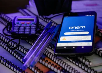 Smartphone exibindo aplicativo do Enem com tela de login gov.br sobre cadernos espirais, canetas azuis e calculadora.