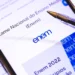 Close de um smartphone exibindo a página oficial do Exame Nacional do Ensino Médio (Enem) no portal gov.br. Sobre a tela, há uma caneta esferográfica de corpo transparente. O fundo é de papel pautado, reforçando o ambiente de estudos.