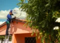 Técnico com capacete azul instala antena parabólica digital do programa Brasil Antenado em telhado de casa laranja.