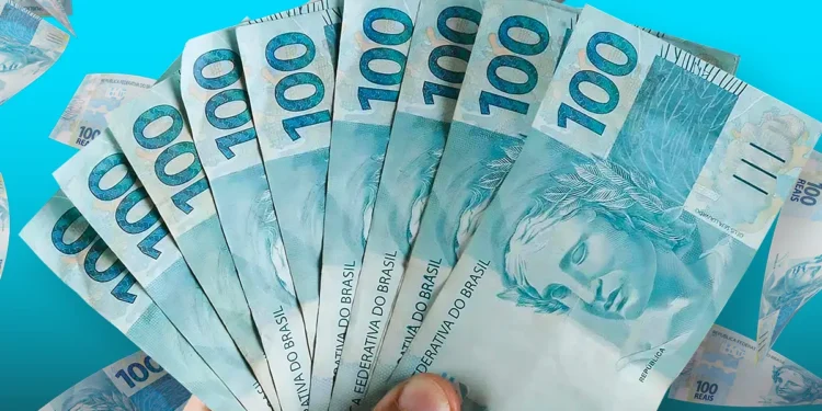 Mão segurando várias notas de 100 reais abertas em leque sobre fundo azul