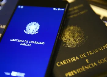 Carteira de Trabalho física ao lado de celular com a versão digital, representando os direitos do trabalhador escalado para o feriado de 1º de maio