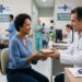 Médico entrega caixa de medicamento a paciente mulher em unidade oncológica do SUS, com outros pacientes ao fundo