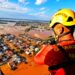 Bombeiro militar com capacete amarelo e colete laranja observa cidade inundada de helicóptero durante operação de resgate