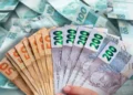 Mão segurando leque de cédulas brasileiras de R$ 50 e R$ 200, com fundo de notas de R$ 100 espalhadas
