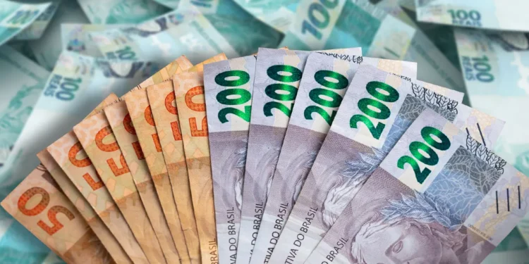 Mão segurando leque de cédulas brasileiras de R$ 50 e R$ 200, com fundo de notas de R$ 100 espalhadas
