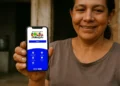 Mulher sorridente mostra celular com tela do aplicativo Bolsa Família da CAIXA, com opções de calendário e acesso