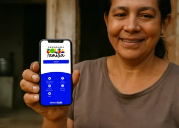Mulher sorridente mostra celular com tela do aplicativo Bolsa Família da CAIXA, com opções de calendário e acesso