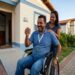 Homem em cadeira de rodas ergue chaves de imóvel sorrindo, ao lado de mulher que o abraça em frente à casa nova
