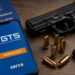 Celular exibe aplicativo FGTS da Caixa sobre mesa com pistola preta, munições, pente e carteira de trabalho azul