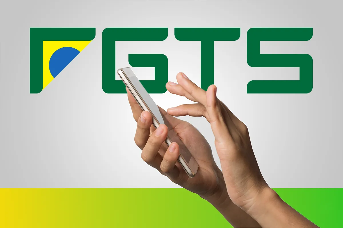 Mãos segurando celular branco com logo verde do FGTS, contendo bandeira brasileira ao fundo