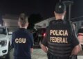 Agentes da CGU e Polícia Federal de costas durante operação noturna com viaturas ao fundo em área residencial