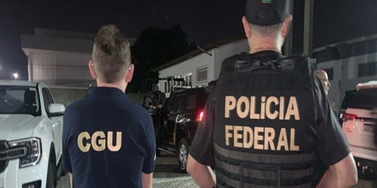 Agentes da CGU e Polícia Federal de costas durante operação noturna com viaturas ao fundo em área residencial