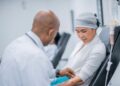 Médico de jaleco branco prepara braço de paciente com lenço na cabeça para infusão intravenosa em ambiente clínico