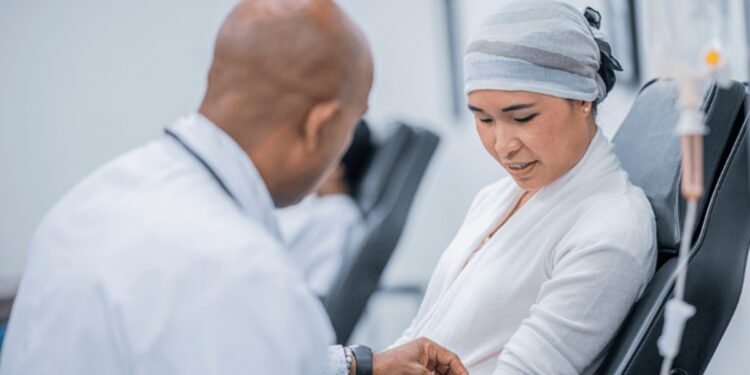 Médico de jaleco branco prepara braço de paciente com lenço na cabeça para infusão intravenosa em ambiente clínico