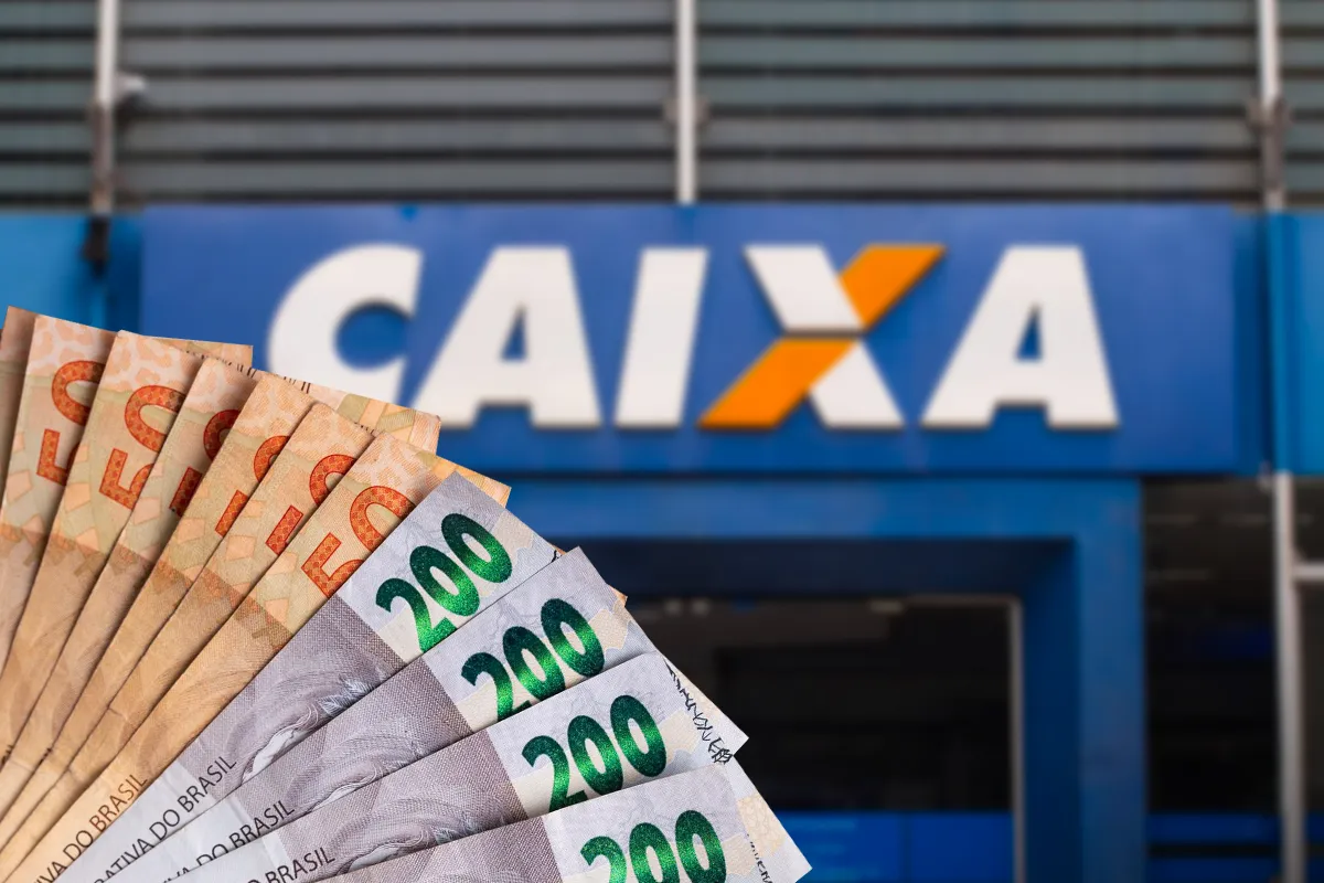 Cédulas de R$ 50 e R$ 200 em leque diante de agência da Caixa.