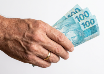 Mão idosa segura 300 reais em notas de R$100.