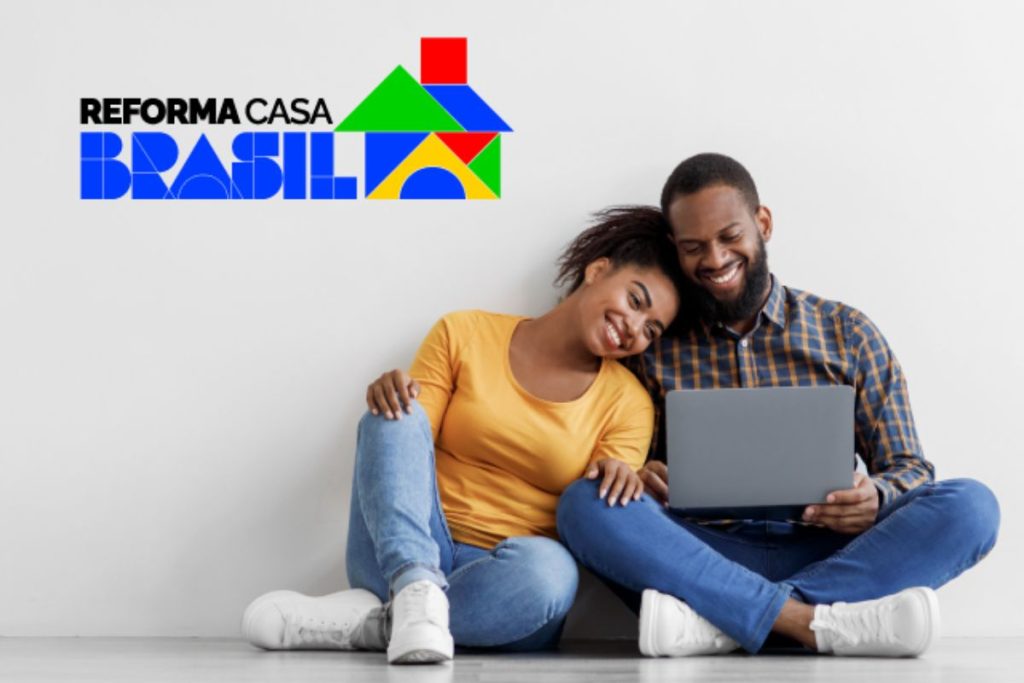 Casal negro sentado no chão com notebook, sorrindo, ao lado do logo Reforma Casa Brasil em cores vivas