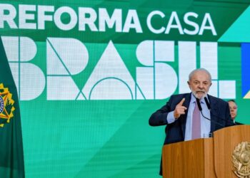 Presidente Lula discursa em púlpito com brasão da República, gesticulando, com painel verde do Reforma Casa Brasil ao fundo