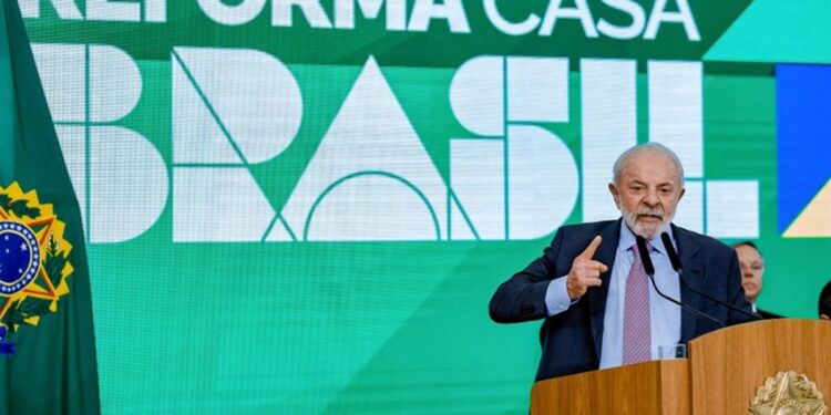 Presidente Lula discursa em púlpito com brasão da República, gesticulando, com painel verde do Reforma Casa Brasil ao fundo