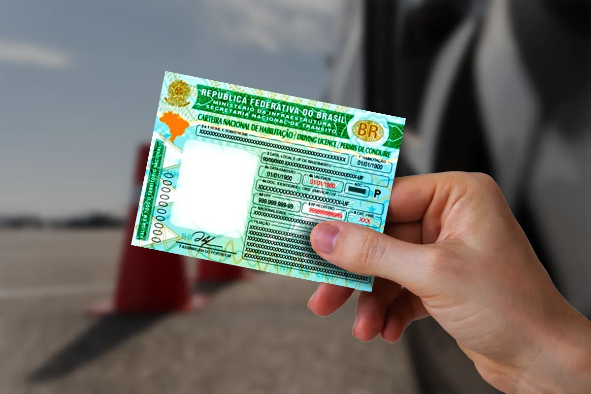 Mão feminina segura Carteira Nacional de Habilitação brasileira com dados fictícios, cones de trânsito vermelhos desfocados ao fundo