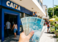 Notas de R$ 100 em frente à agência Caixa em rua comercial.