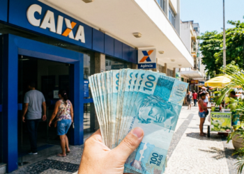 Notas de R$ 100 em frente à agência Caixa em rua comercial.