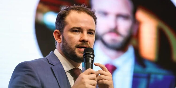 Dario Durigan, ministro da Fazenda, segura microfone durante entrevista, vestindo terno cinza