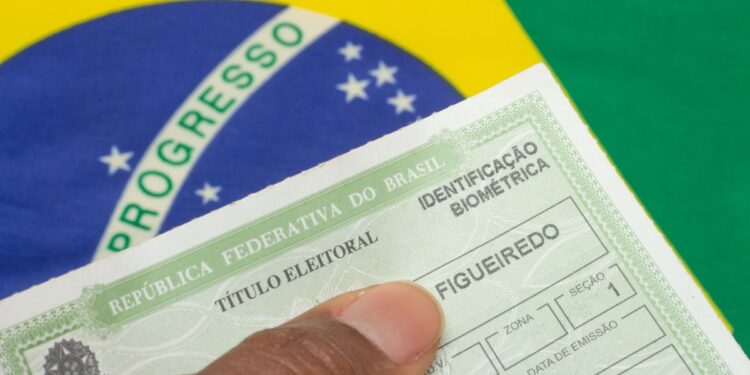 Título eleitoral biométrico com bandeira do Brasil ao fundo.