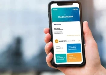Mão segura smartphone com aplicativo FGTS da Caixa aberto, mostrando saldo e opções de saque-aniversário e imediato