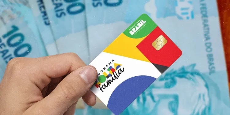 Cartão do Bolsa Família sendo segurado na mão com notas de R$ 100 ao fundo