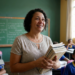 Professora segura livros didáticos em sala de aula com alunos uniformizados