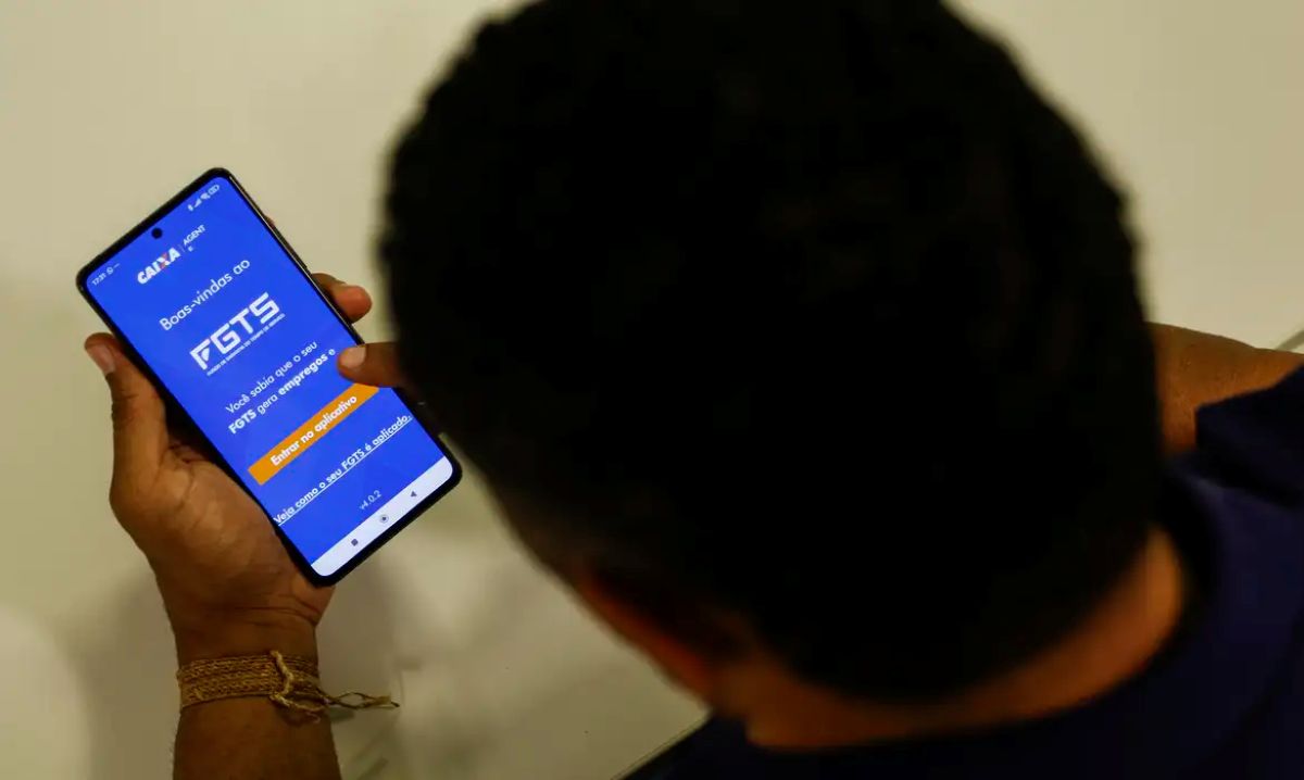 Pessoa olha para o celular aberto no aplicativo FGTS da Caixa, na tela de boas-vindas