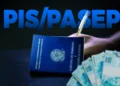 Carteira de trabalho e cédulas de cem reais sobre uma mesa, com a inscrição PIS/Pasep ao fundo, em referência ao ressarcimento das cotas do antigo fundo em 2026.