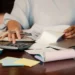 Desenrola Brasil 2.0: imagem ilustrativa de pessoa organizando boletos com calculadora, notebook e caderno, em referência ao processo de simulação de descontos previstos no programa de renegociação de dívidas