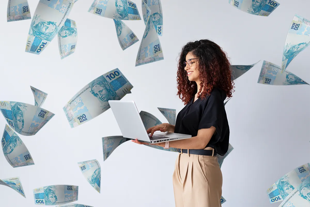 Uma mulher sorridente com cabelos cacheados e óculos utiliza um notebook. Ao seu redor, cédulas de cem reais flutuam sobre um fundo claro, simbolizando alívio financeiro e economia.