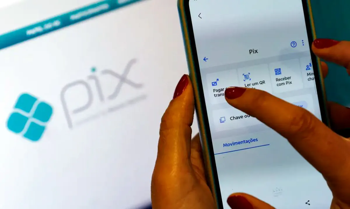 Mãos segurando smartphone com aplicativo bancário aberto na função Pix, destacando riscos de golpes e fraudes em transferências digitais.