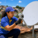 Técnica uniformizada instala antena parabólica no telhado com casas ao fundo