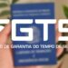 Logotipo do FGTS sobre imagem de mão segurando a carteira de trabalho