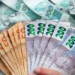 Notas de reais espalhadas com dinheiro sendo segurado em primeiro plano