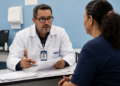 Perito médico do INSS de jaleco branco conversa com uma segurada à mesa durante atendimento de perícia