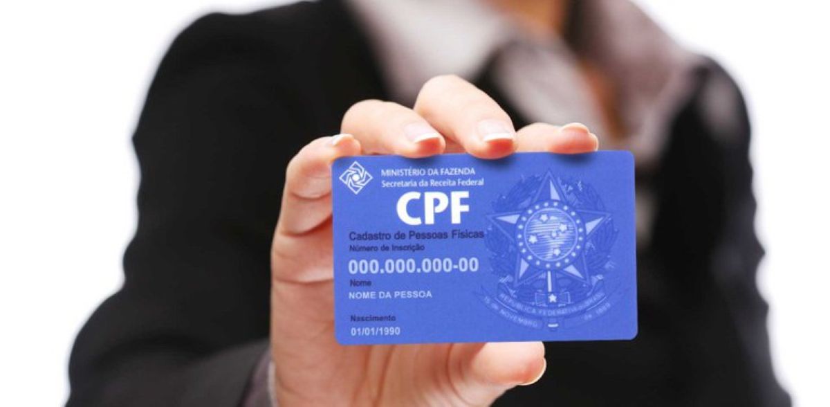 Mão segura um cartão de CPF azul e, ao redor, uma pessoa de terno