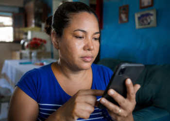 Mulher utiliza o celular sentada no sofá da sala de casa