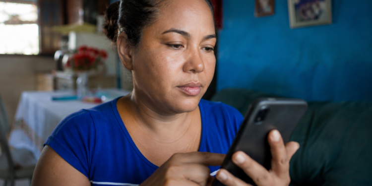 Mulher utiliza o celular sentada no sofá da sala de casa