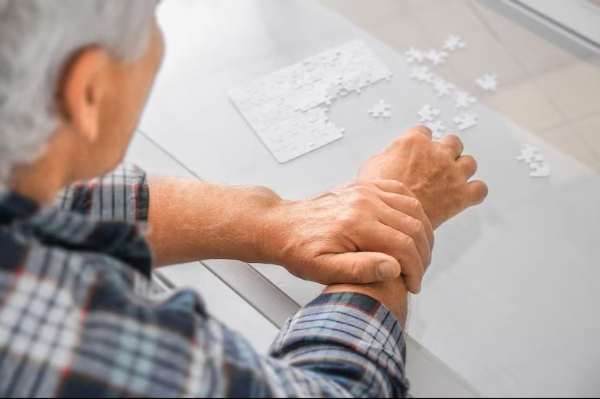 Homem idoso segura o próprio punho diante de um quebra-cabeça branco sobre a mesa